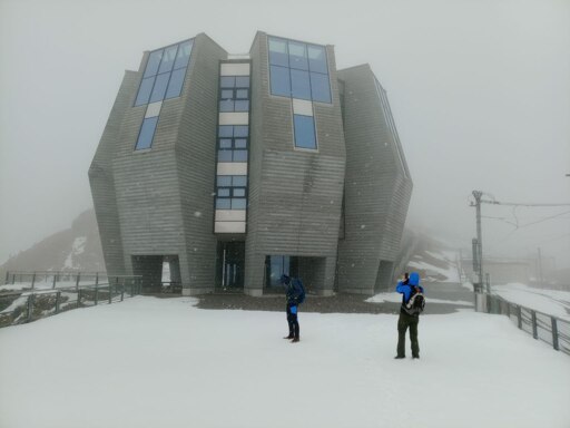 Snow, lots of snow, a building 8 sides, and walls that are inclined outside towards mid-height, then go back. Two people dressed in mountain apparel in the middle.